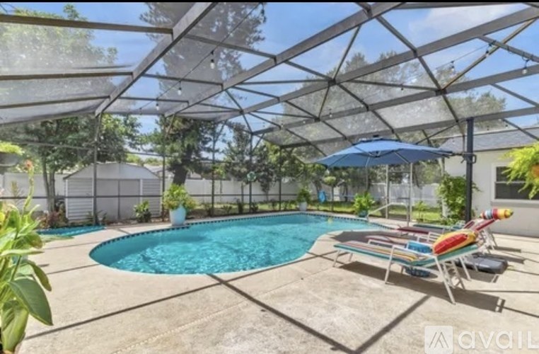 A pool under a glass roof with sun loungers and a blue umbrella.