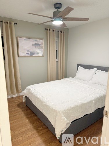 A bedroom with a bed, a ceiling fan, and a painting on the wall.