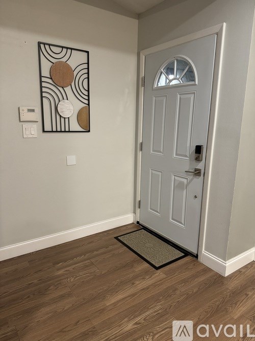 A white door with a glass window is in a room with a wooden floor and a picture on the wall.