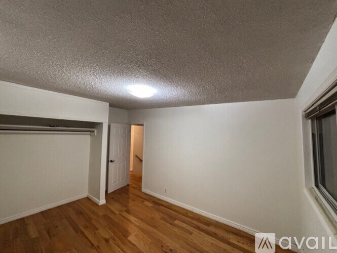 A room with wooden floors and white walls, with a window on the right side.