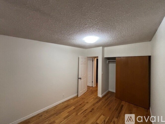 A room with wooden floors and white walls, with a door on the left and a wooden cabinet on the right.