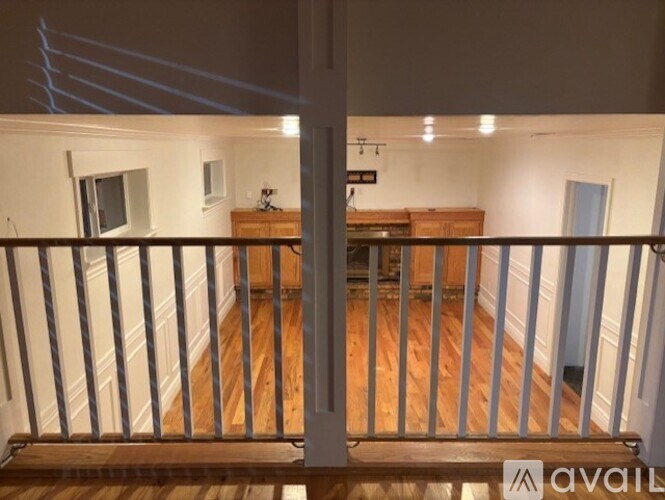 A balcony with a railing and a view of a room with a wooden floor and a cabinet.