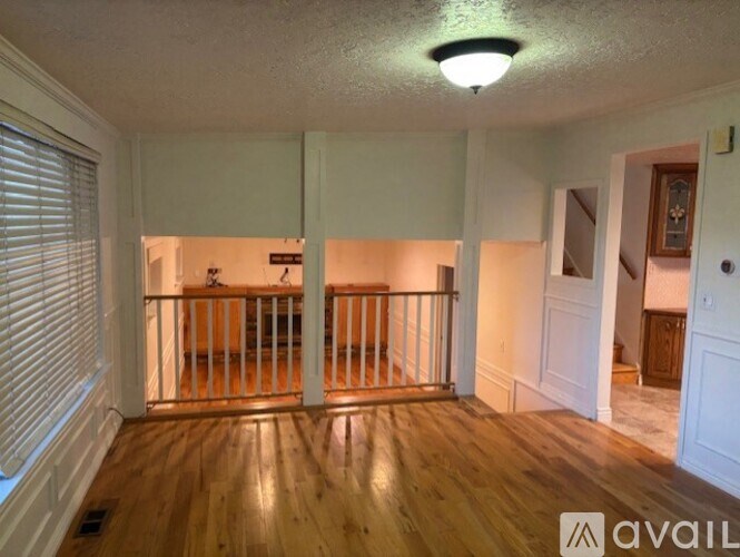 A room with wooden floors and white walls, with a window on the left and a door on the right.