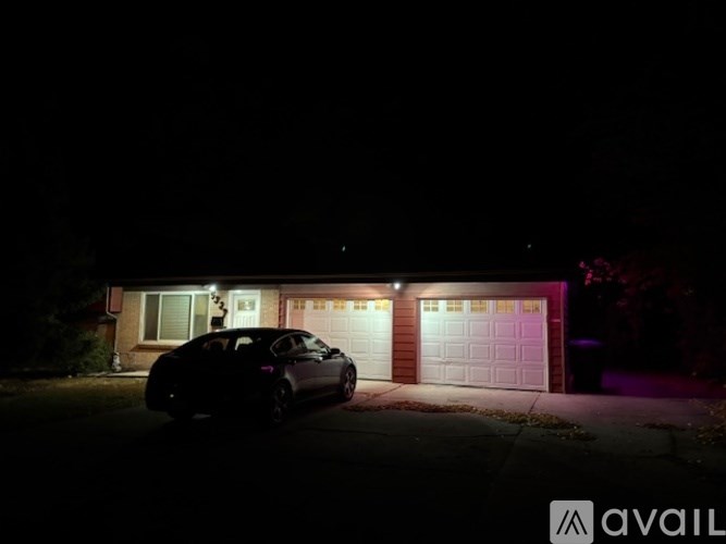A black car is parked in front of a house with garage doors.