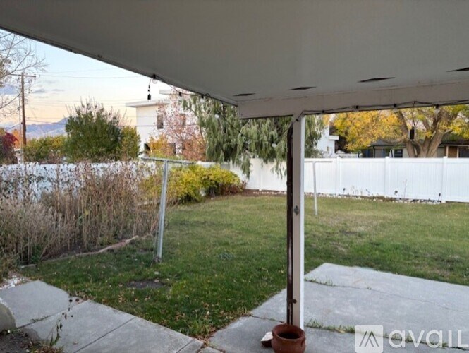 A patio with a white awning over it and a view of a backyard with a white fence.