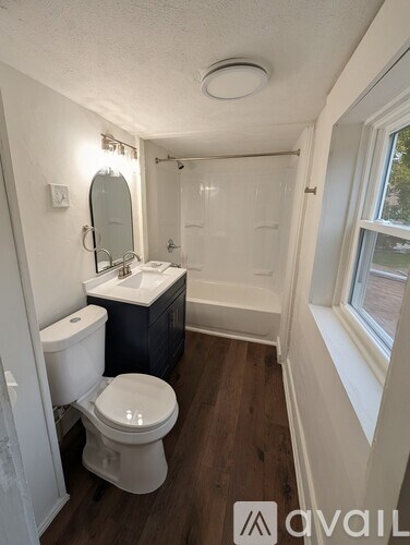 A bathroom with a toilet, sink, mirror, and window.