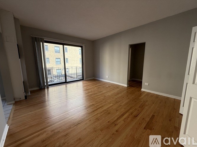 A spacious room with wooden flooring and a large window with a view of a building outside.