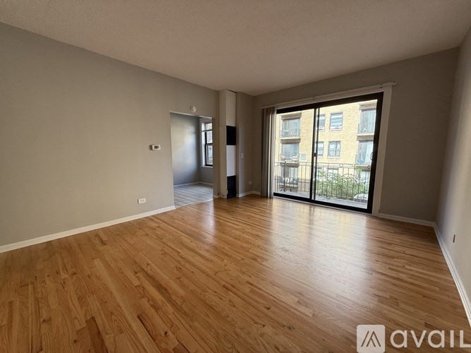 A spacious room with wooden flooring and a sliding glass door leading to a balcony.