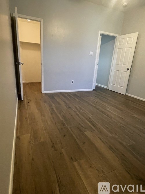 A room with wooden flooring and two doors, one of which is open.