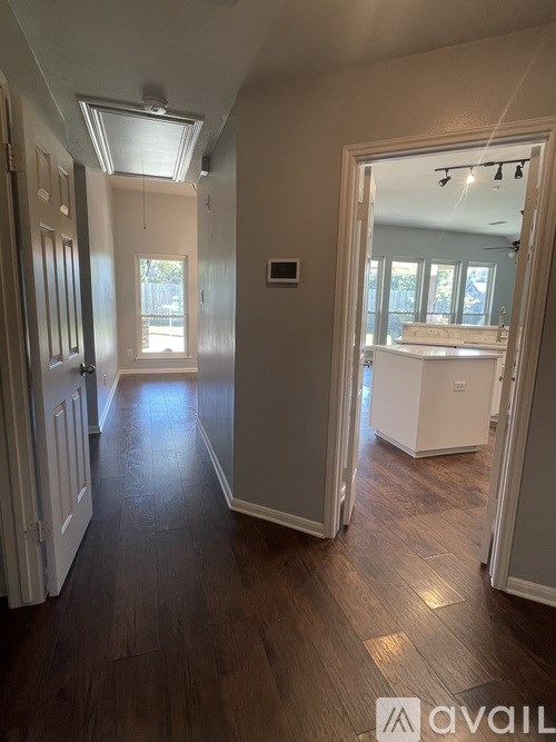 A hallway with wood floors and white walls leading to a kitchen.