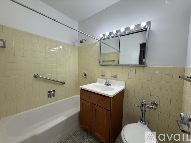 A bathroom with a white sink, a white toilet, a white bathtub, and a mirror with lights above it.