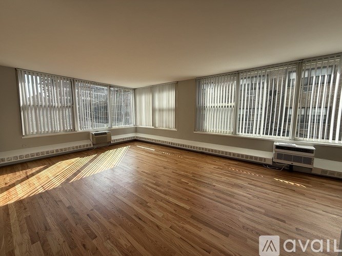 A room with wooden flooring and large windows with blinds.