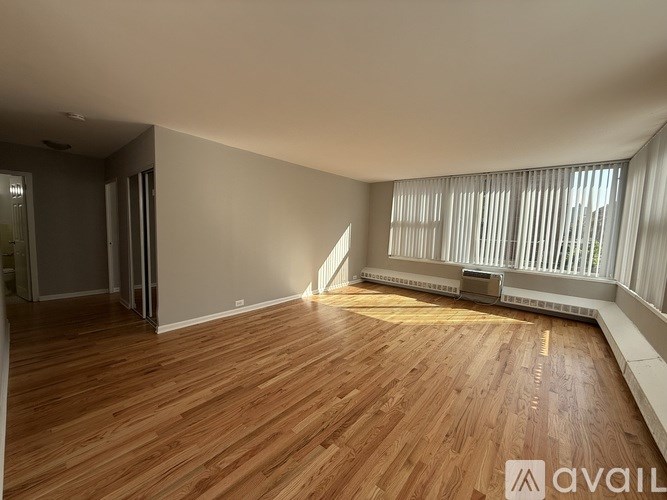 A spacious room with wooden flooring and a window with blinds.