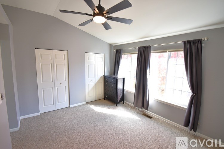 A room with a ceiling fan and a window with curtains.