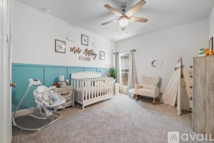 A baby nursery with a white crib, rocking chair, and a teal accent wall.