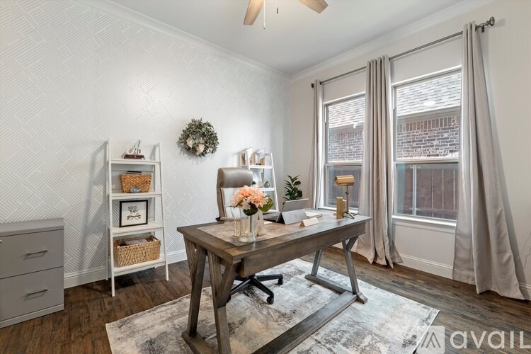 A room with a wooden desk and a chair, a wreath on the wall, and a window with curtains.
