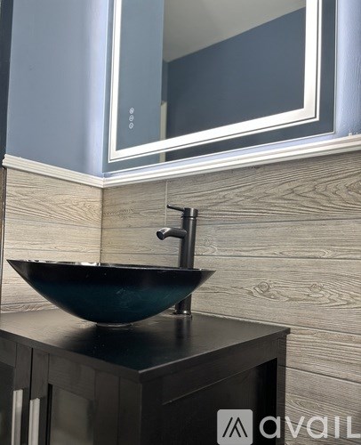 A black sink with a silver faucet on a wooden cabinet.