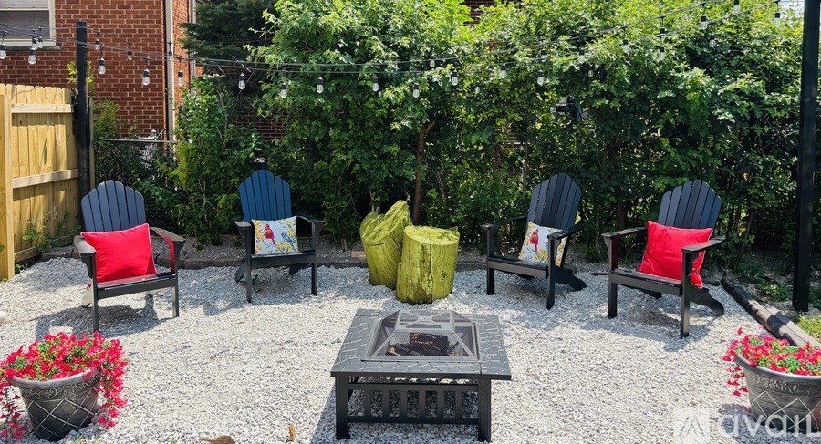 A set of four Adirondack chairs are arranged around a fire pit in a gravel courtyard.