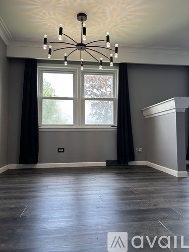 A room with a chandelier, a window with curtains, and a wooden floor.