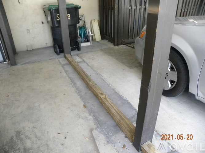 A car is parked in a garage next to a black trash can.