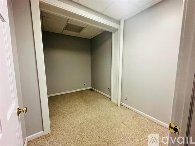 A room with carpeted floor and white walls, with a door on the left and a window on the right.