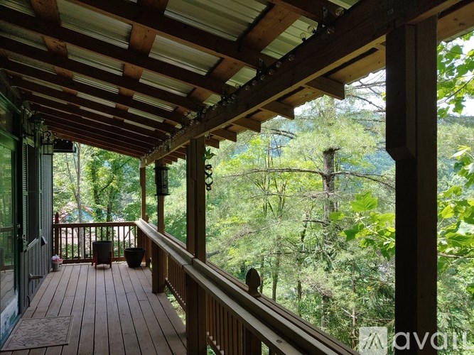A wooden deck with a railing and a table with chairs is surrounded by trees.