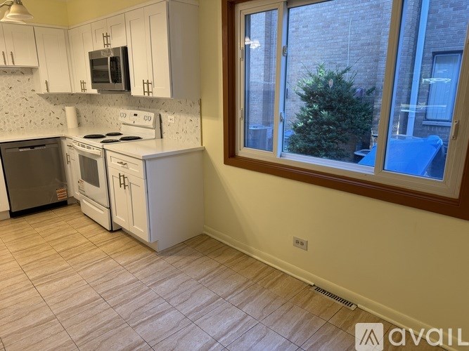 A kitchen with white appliances and cabinets, a window, and a tiled floor.