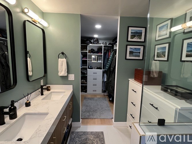 A bathroom with a sink, mirror, and a closet with clothes.