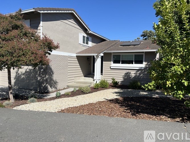 A house with a grey roof and a white door is surrounded by greenery.