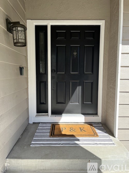 A black door with a glass panel and a doormat with letters P&K on it.