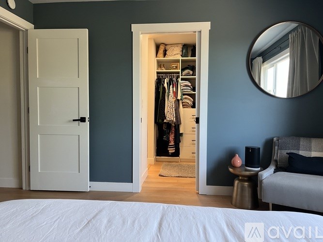 A bedroom with a white bed and a wardrobe with clothes hanging in it.