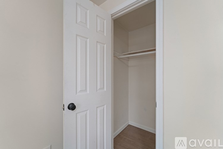 A white door with a black handle is open to a small, empty room with a shelf.