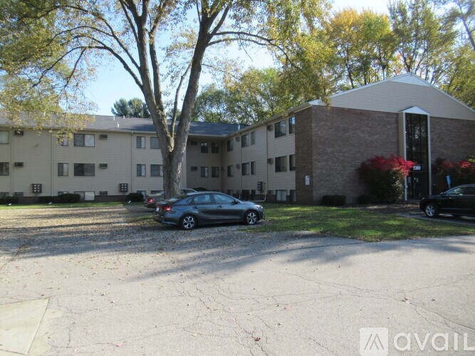 A parking lot in front of a brick building with a tree and a car.