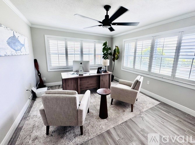 A room with a desk, chairs, and a ceiling fan.