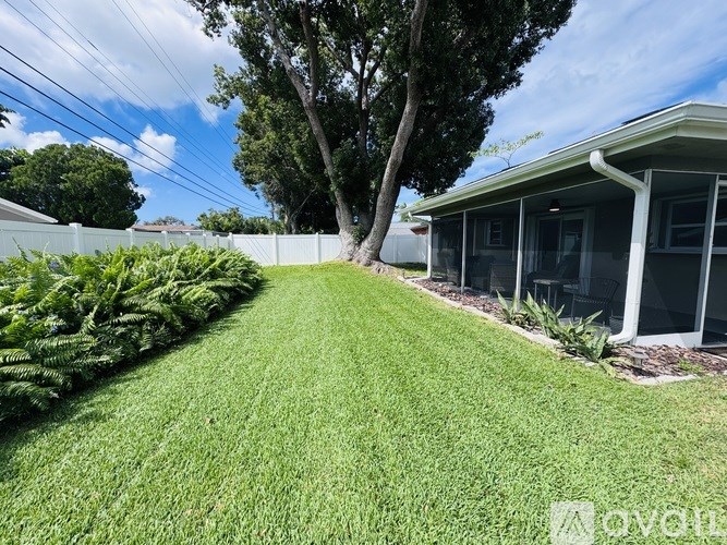 A well-maintained lawn leads to a house with a white fence and a tree in the background.