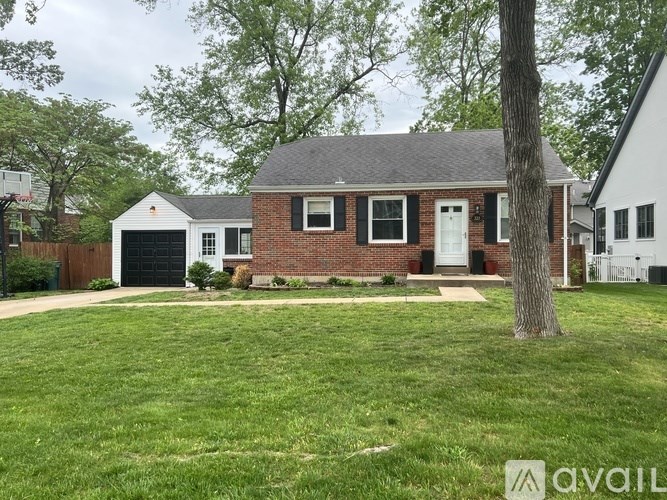 A house with a red brick exterior and a white door is surrounded by a well-kept lawn.