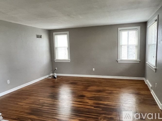 A room with wooden flooring and two windows.