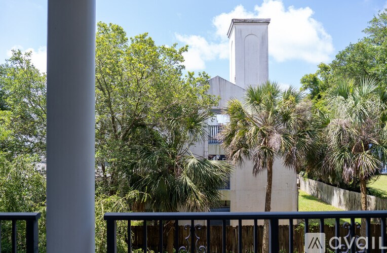 A white tower stands behind a fence with trees in the foreground.