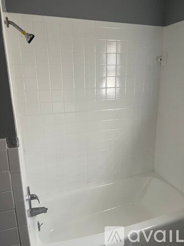 A white tiled shower area with a shower head and faucet.