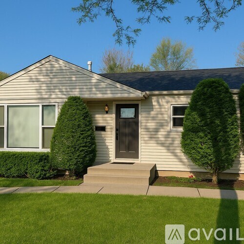 A house with a grey siding and a black door is surrounded by green bushes.