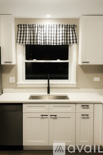 A kitchen with white cabinets and a checkered curtain.