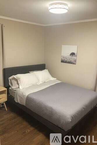 A bedroom with a bed, nightstand, and a picture of a field on the wall.