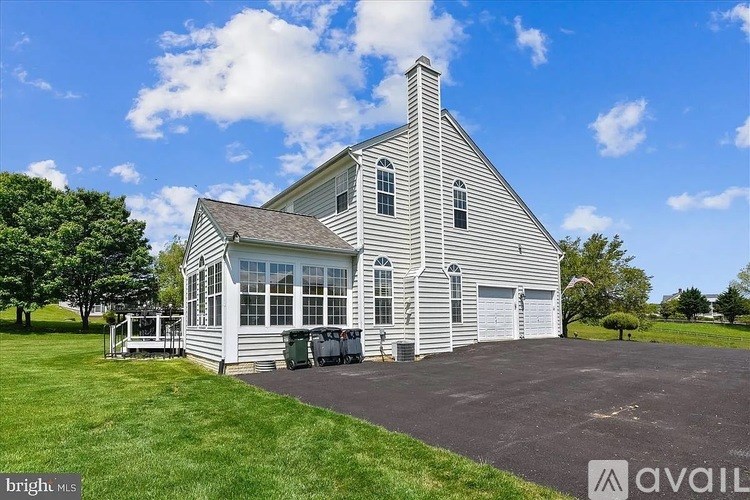 A large white house with a grey roof and a chimney is surrounded by a green lawn.