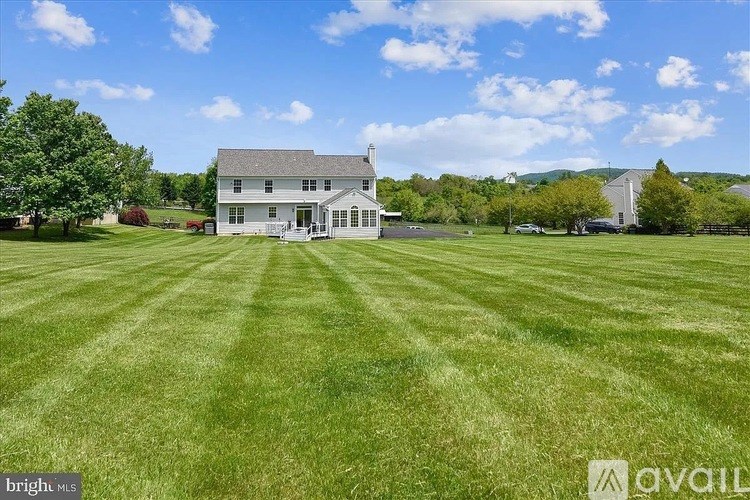 A large white house with a grey roof is surrounded by a green lawn.