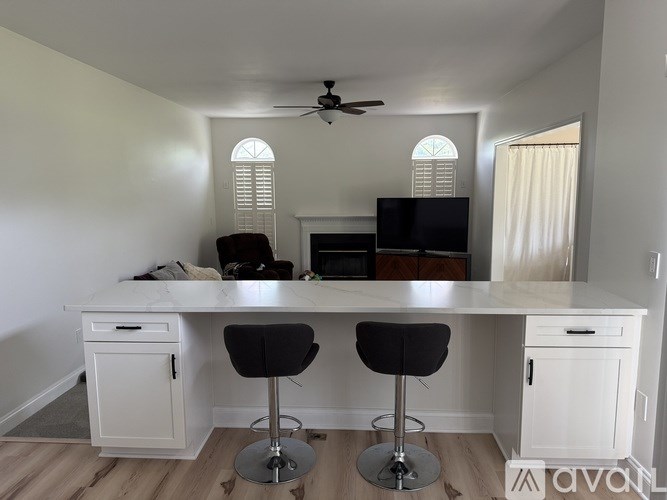 A white desk with two chairs and a television in a room.