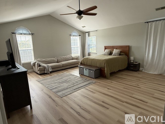 A bedroom with a bed, a couch, a television, and a ceiling fan.
