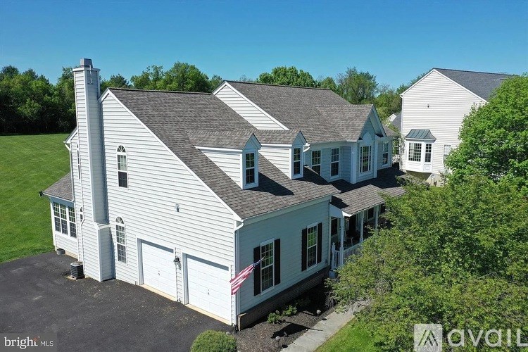 A large white house with a grey roof and a chimney is surrounded by greenery.