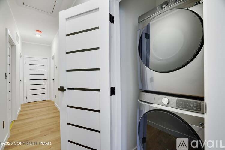 A white washing machine is in a small, white-walled laundry room.