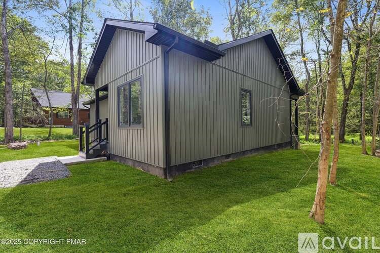 A house with a grey exterior is surrounded by a grassy lawn and trees.