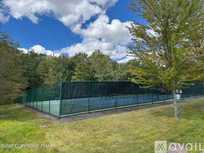A tennis court is enclosed by a green fence and surrounded by trees.